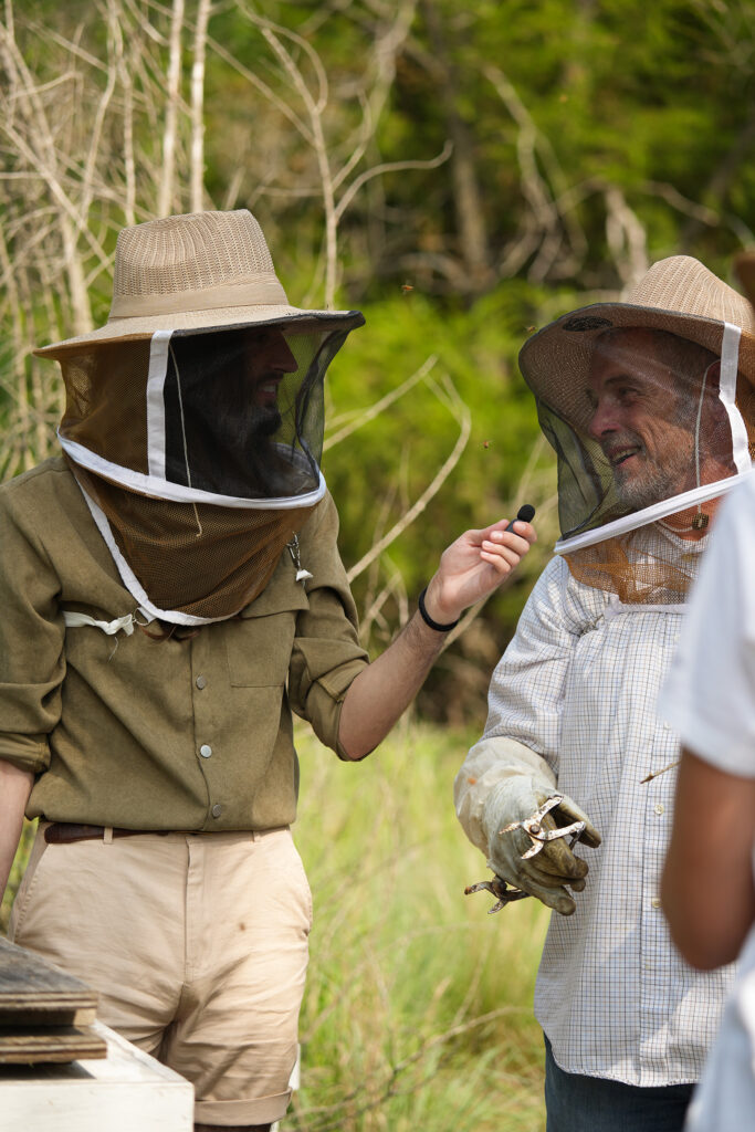 Two men talk wearing beekeeping hats. 